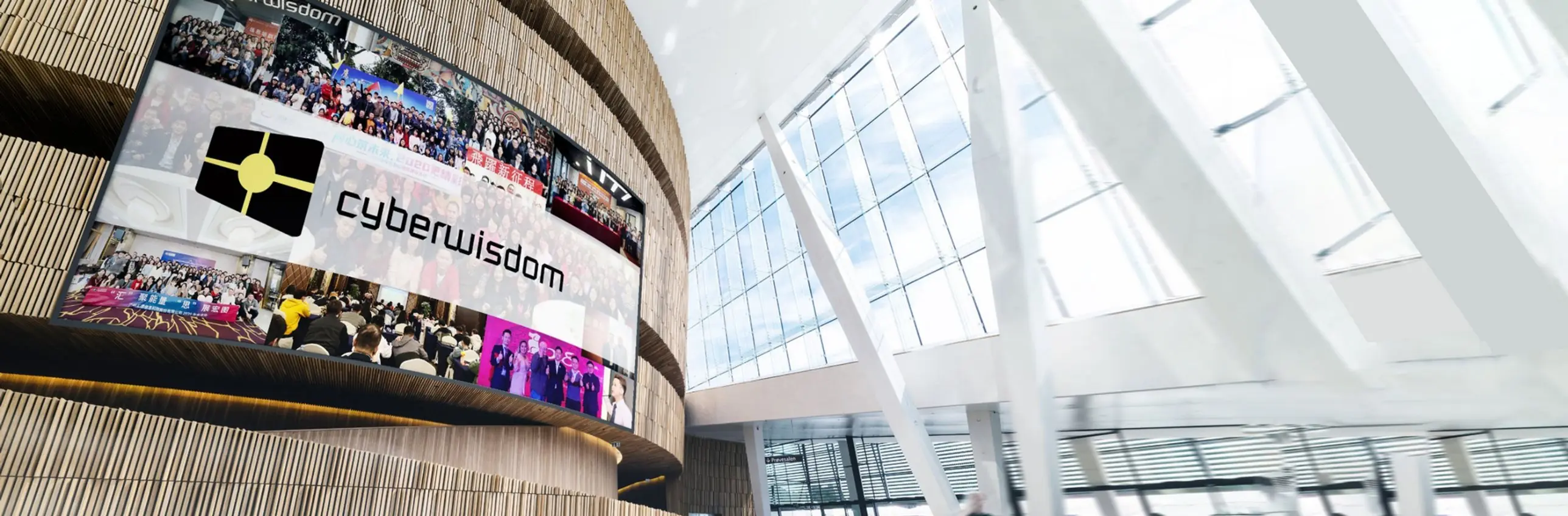 Cyberwisdom logo on a large curved display showing photos of company events, inside a bright modern atrium